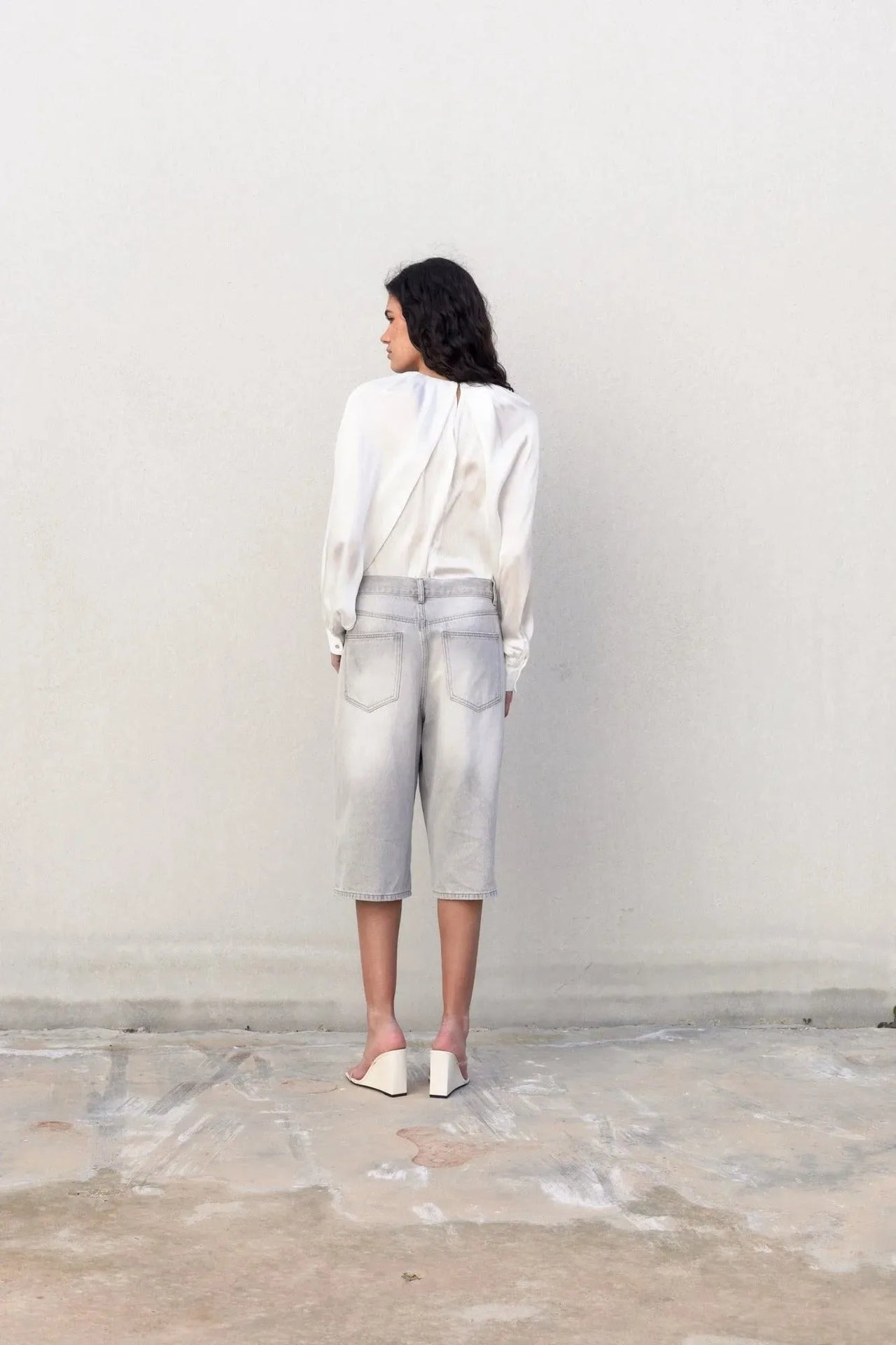 Femme de dos en blouse satin élégante, affichant un look chic et décontracté avec un pantalon en jean.