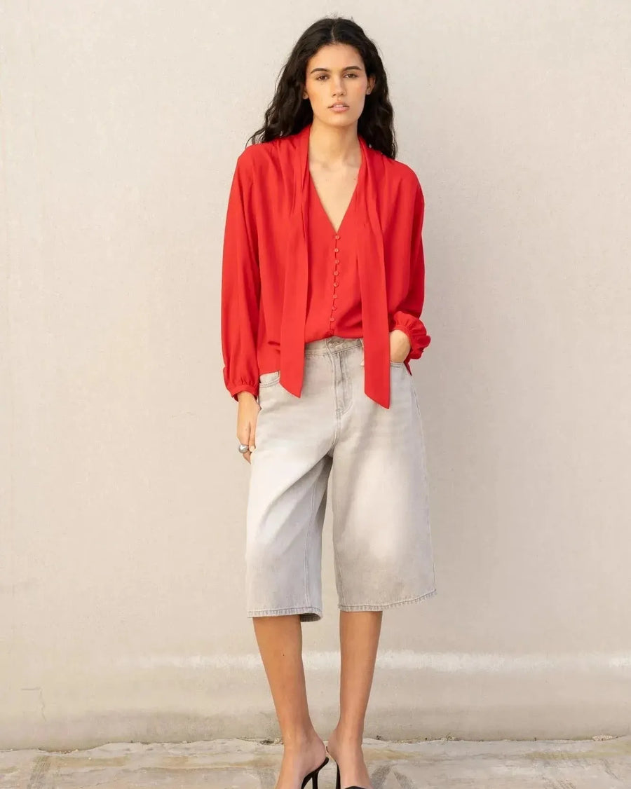 Vue frontale d'un chemisier col lavallière femme rouge fluide à manches longues, stylisé avec un pantalon ample et des sandales.