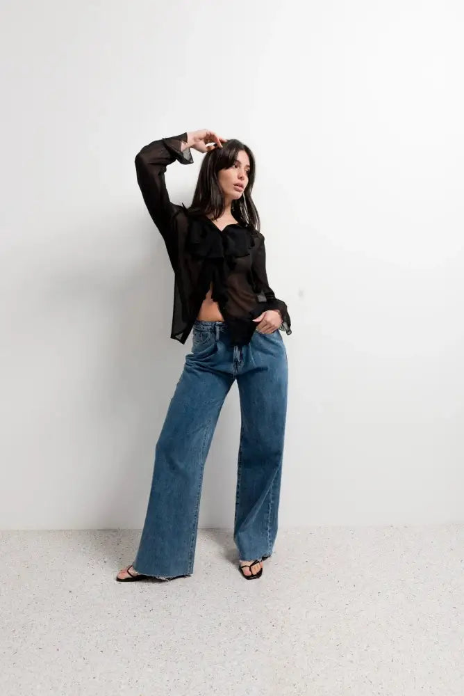 Chemisier noir transparent femme chic avec volants et voile fluide, porté avec jeans wide-leg