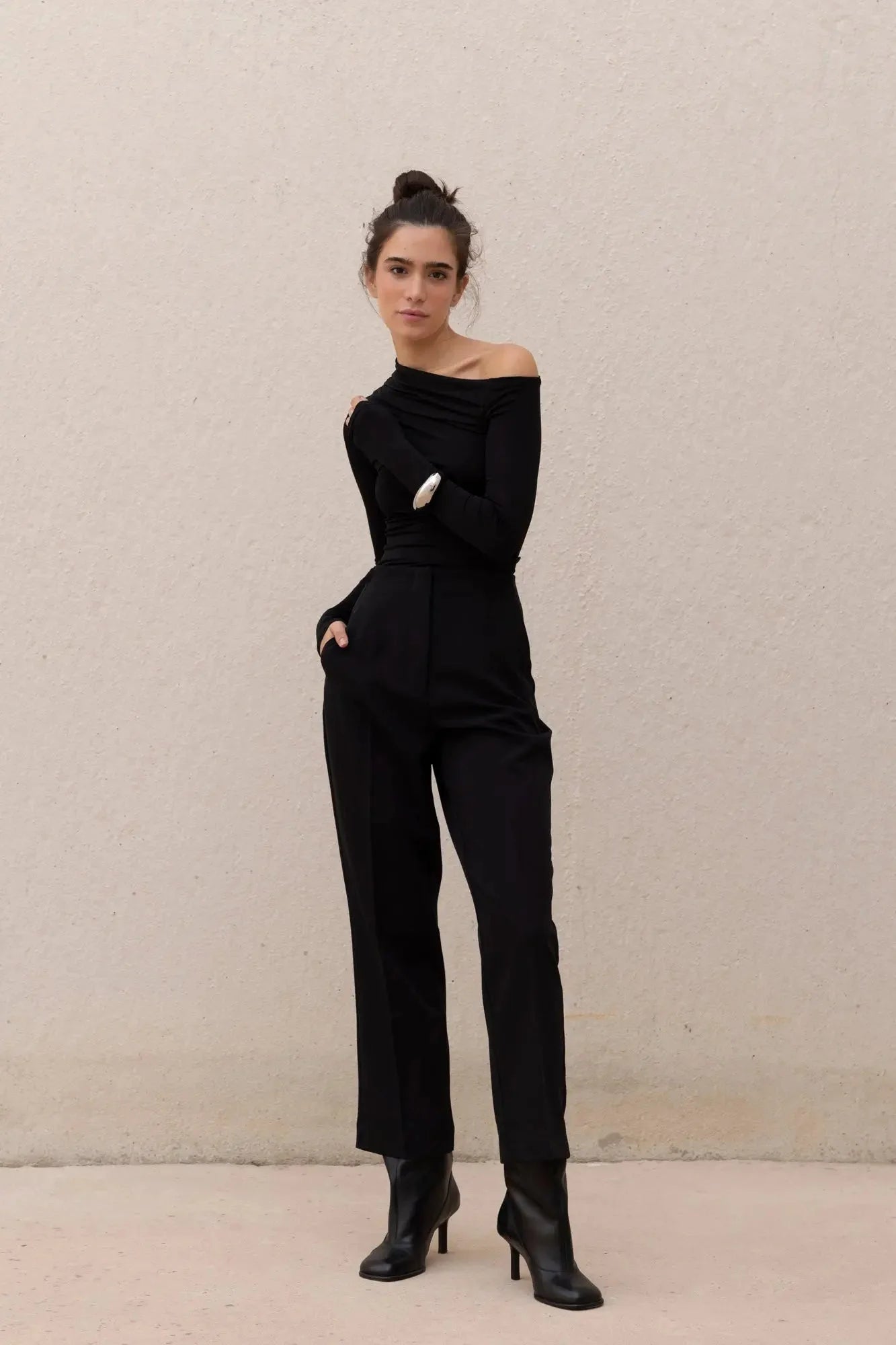 Femme portant un pantalon pinces noir, confort exceptionnel, haut off-shoulder et bottines