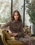 Femme assise dans un décor élégant, portant une veste blazer leopard femme, style unique avec imprimé animal.