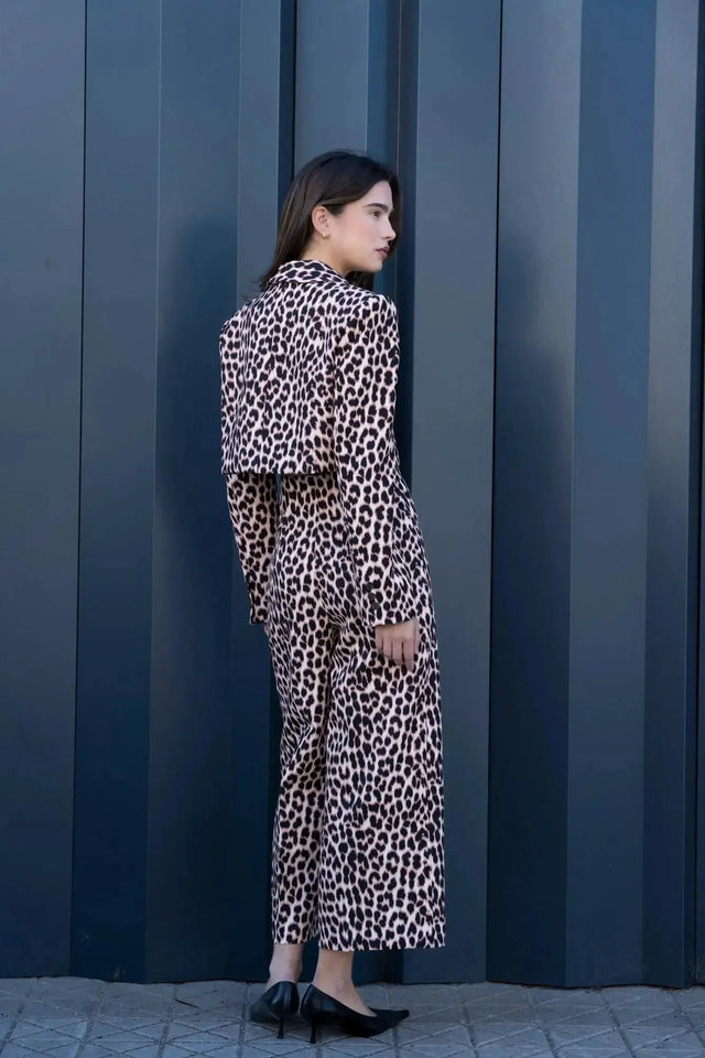 Vue arrière d'une femme portant une veste blazer leopard femme, style unique avec imprimé animal, devant un mur contemporain.