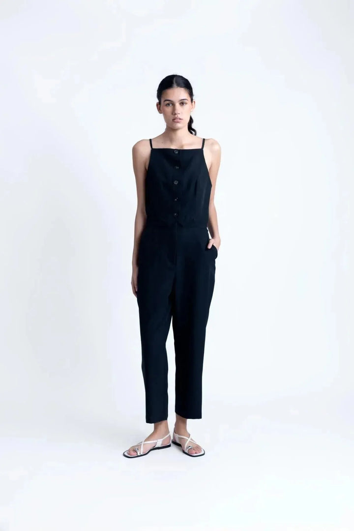 Combinaison noire élégante à boutons pour femme, modèle chic avec bretelles fines, parfaite pour une allure moderne.