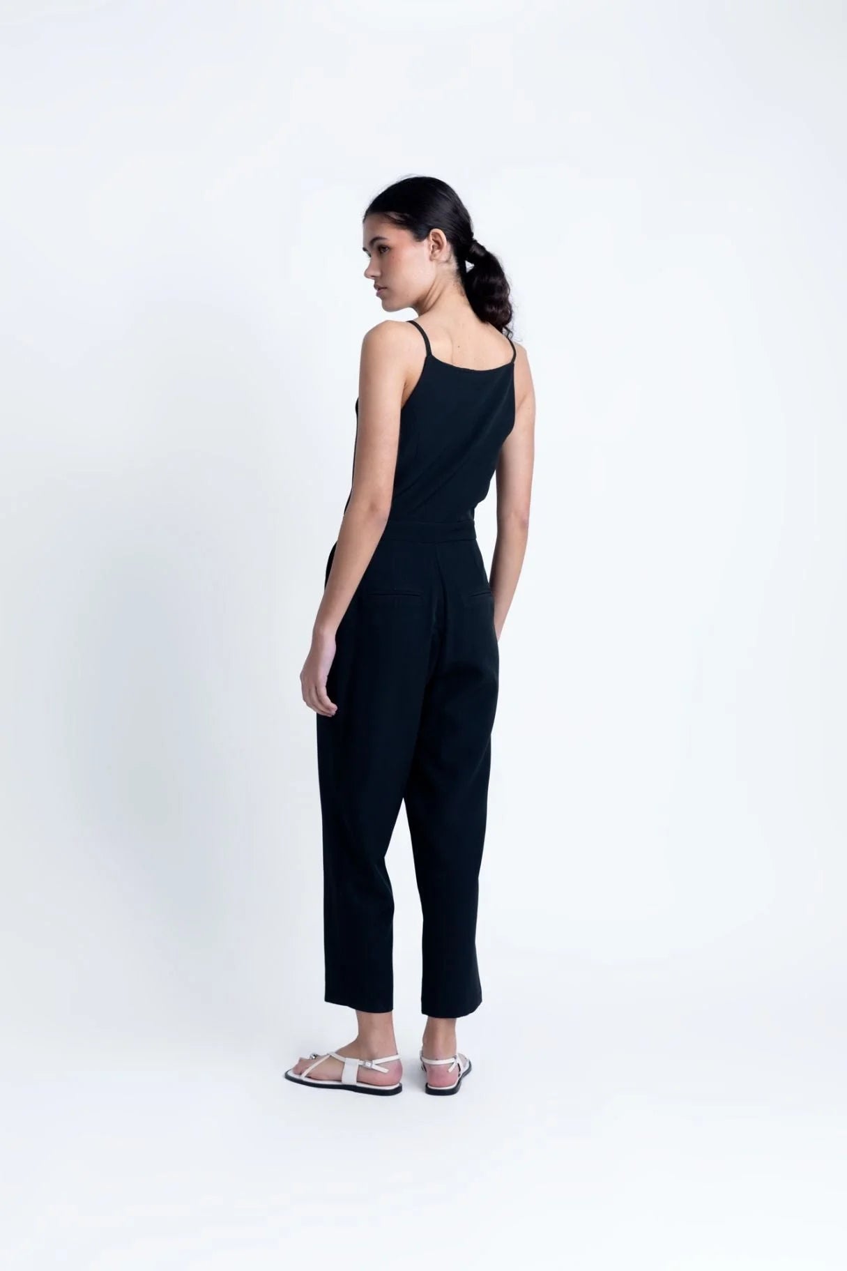 Femme en combinaison noire élégante à bretelles, pantalon fluide, sandales plates