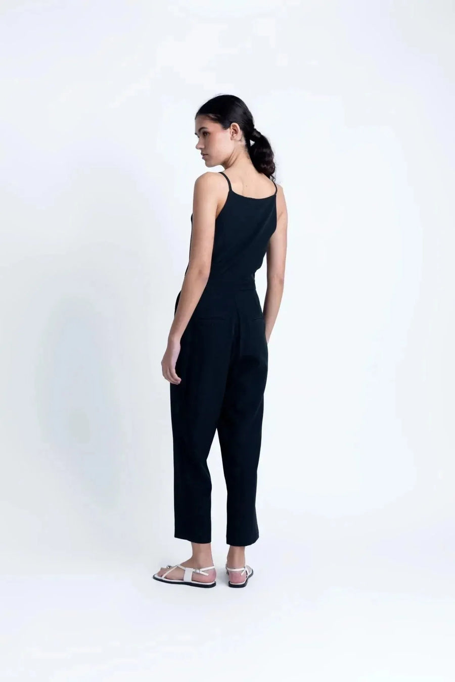 Vue arrière de la combinaison noire femme, soulignant le design chic et les poches discrètes, essentielle pour un look sophistiqué.