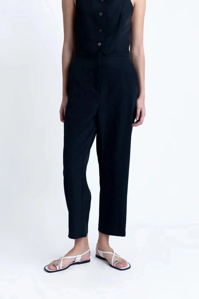 Détails du bas de la combinaison noire élégante à boutons, montrant le pantalon droit et la taille haute, parfaite pour le travail ou les soirées.