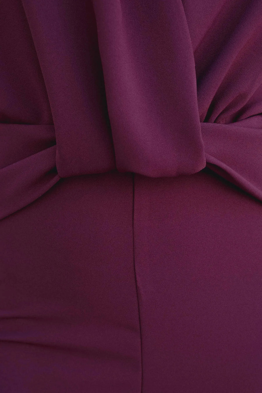Femme montrant le dos nu d'une combinaison chic pour femme bordeaux prune à encolure licou avec de grandes boucles d'oreilles argentées.