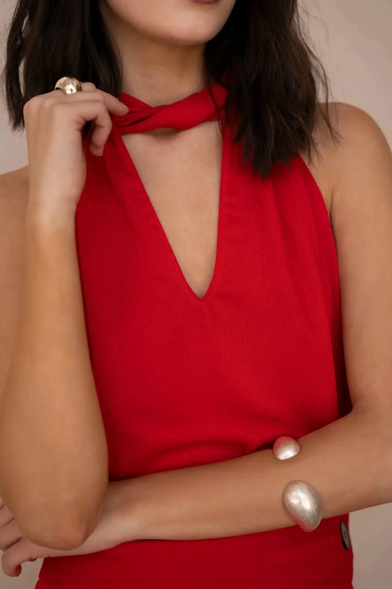 Haut rouge femme chic col noué, décolleté profond pour un look élégant, porté par une femme montrant son accessoire.