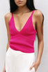 Femme portant un pull crop top fuchsia en maille côtelée à décolleté V profond et bretelles fines, accompagné de pantalons clairs.