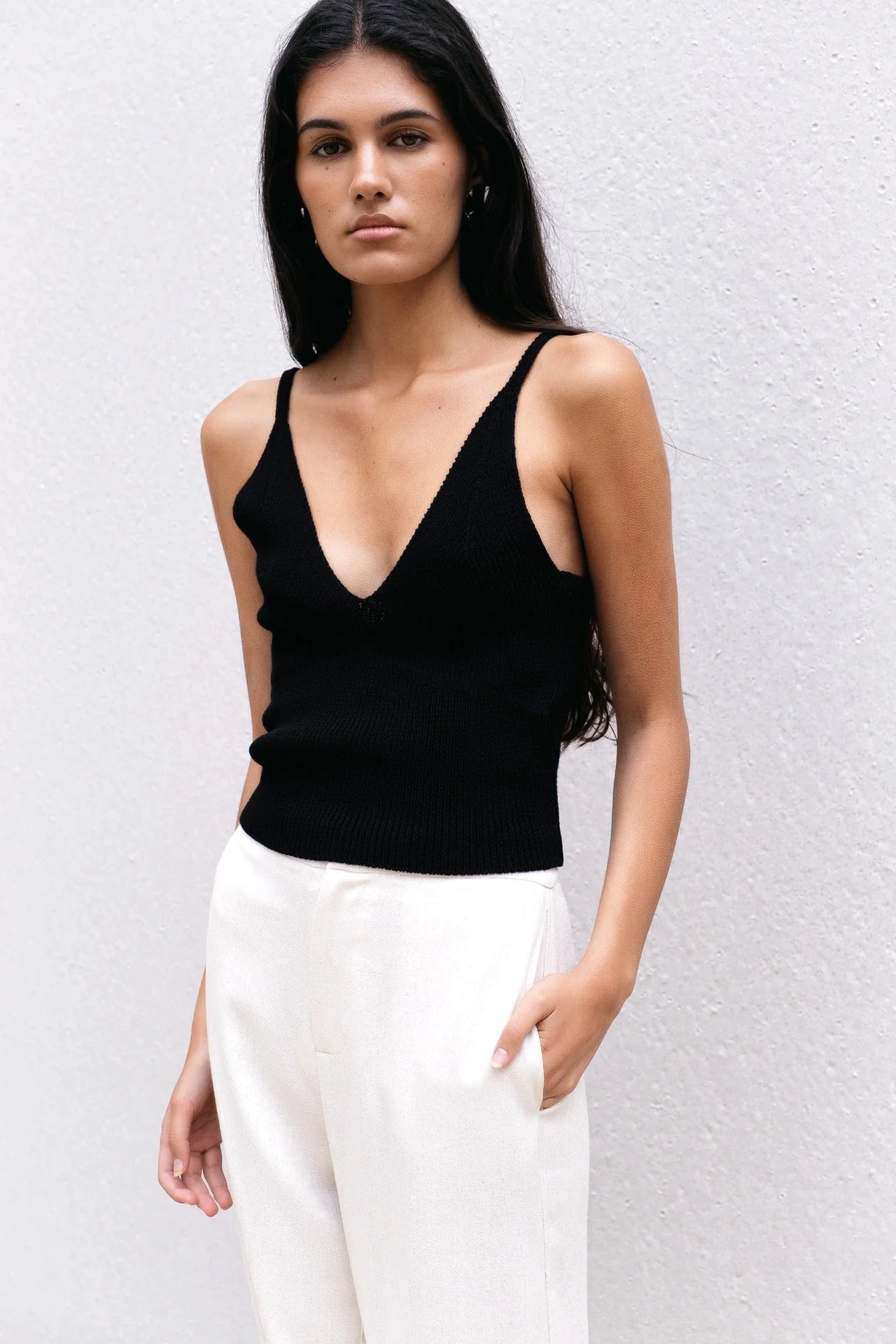 Modèle féminin affichant un pull crop top noir en maille côtelée à décolleté V, associé à une allure sophistiquée et moderne.