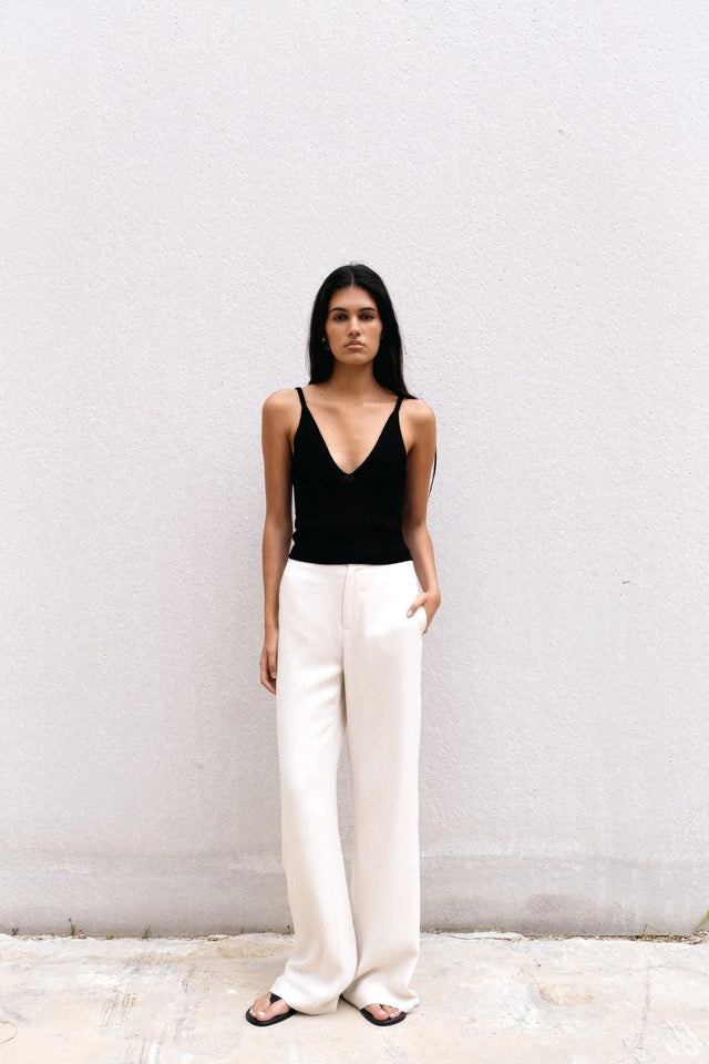 Femme dans un pull crop top noir en maille côtelée, se tenant contre un mur, avec des détails de bretelles fines.