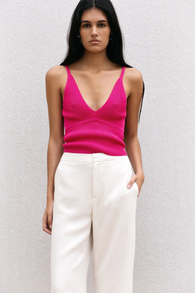 Femme affichant un pull crop top fuchsia en maille côtelée à décolleté V profond et bretelles fines, avec un style chic et lumineux.