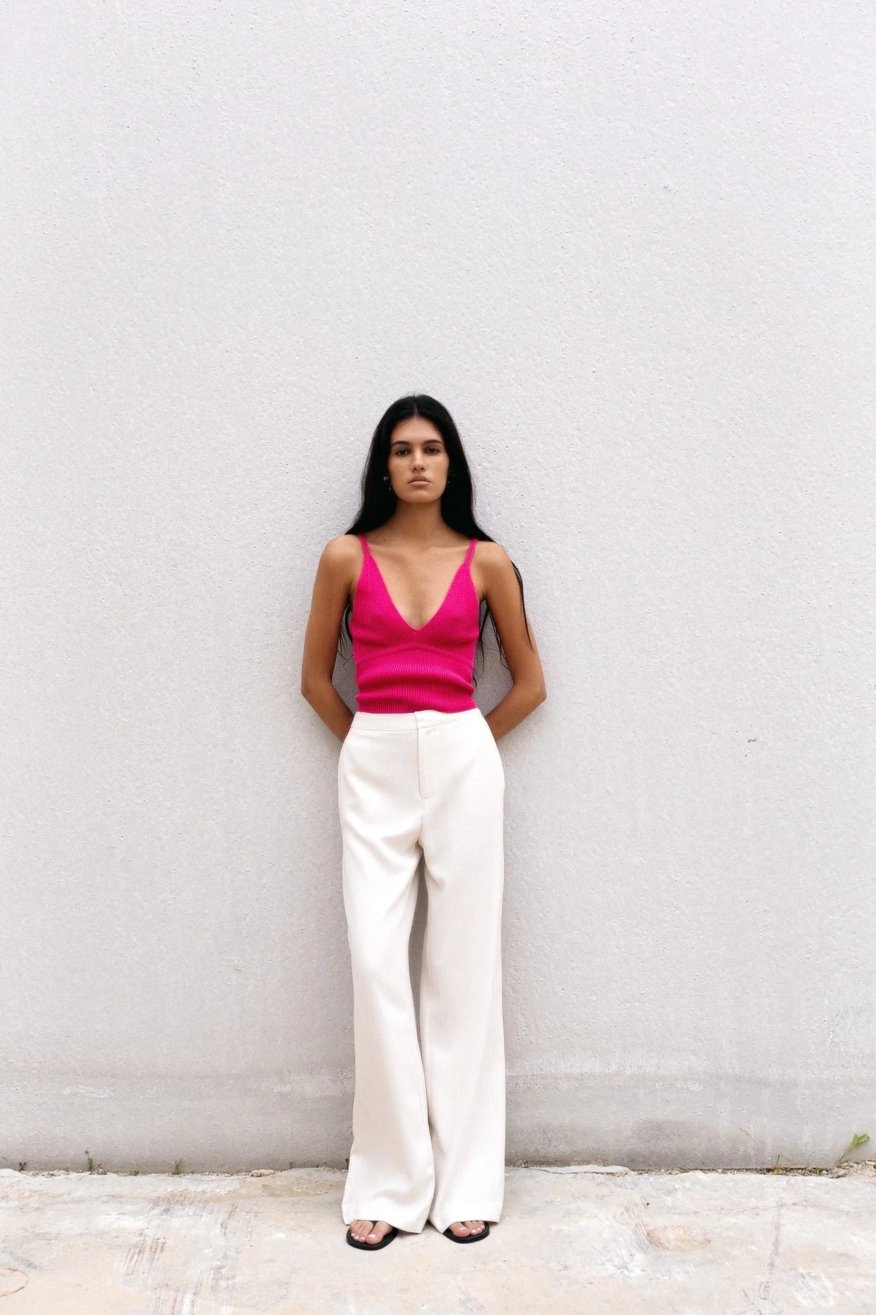 Femme devant un mur avec un pull crop top fuchsia en maille côtelée et un décolleté V, créant une silhouette élégante.