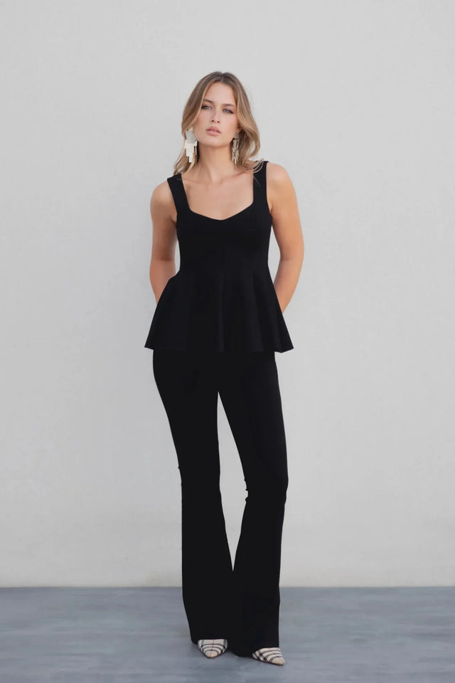 Pantalon Évasé Noir Sapiato: Élégance Confortable pour Toutes Occasions avec un modèle qui porte un haut noir stylé et le pantalon évasé noir, posant dans un décor minimaliste.