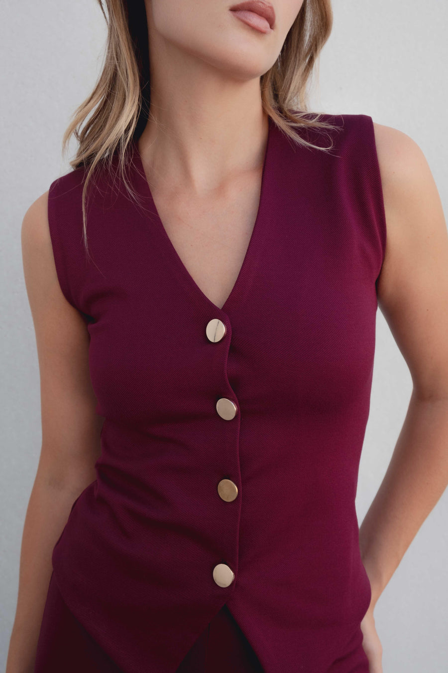 Débardeur tricot femme bordeaux à boutons dorés, mettant en avant le décolleté en V et la coupe ajustée.