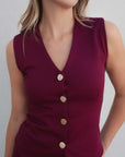 Débardeur tricot femme bordeaux à boutons dorés, mettant en avant le décolleté en V et la coupe ajustée.