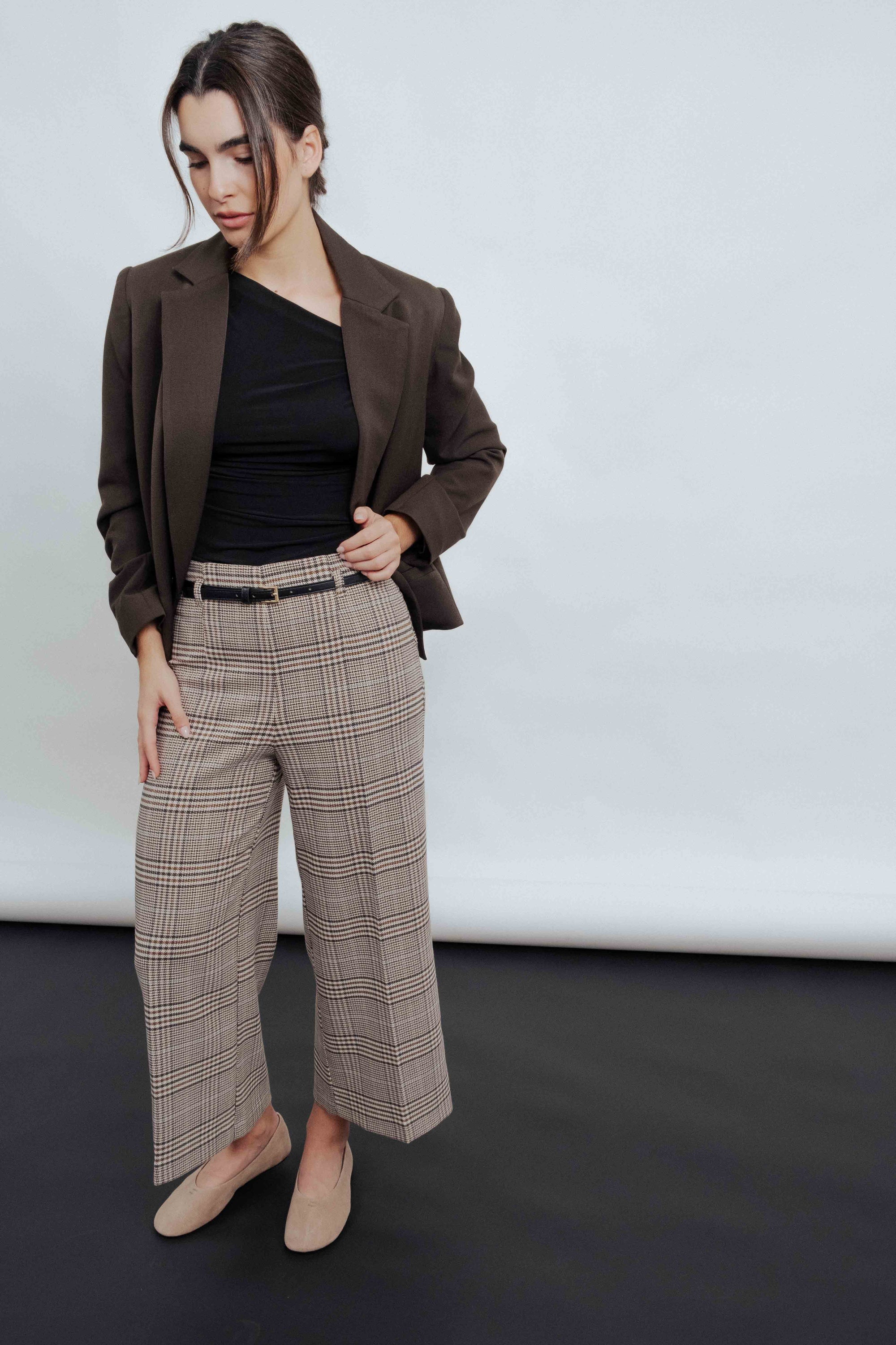 Femme portant un Pantalon culotte à carreaux marron, associé à un blazer et un top noir, offrant un look moderne et sophistiqué.