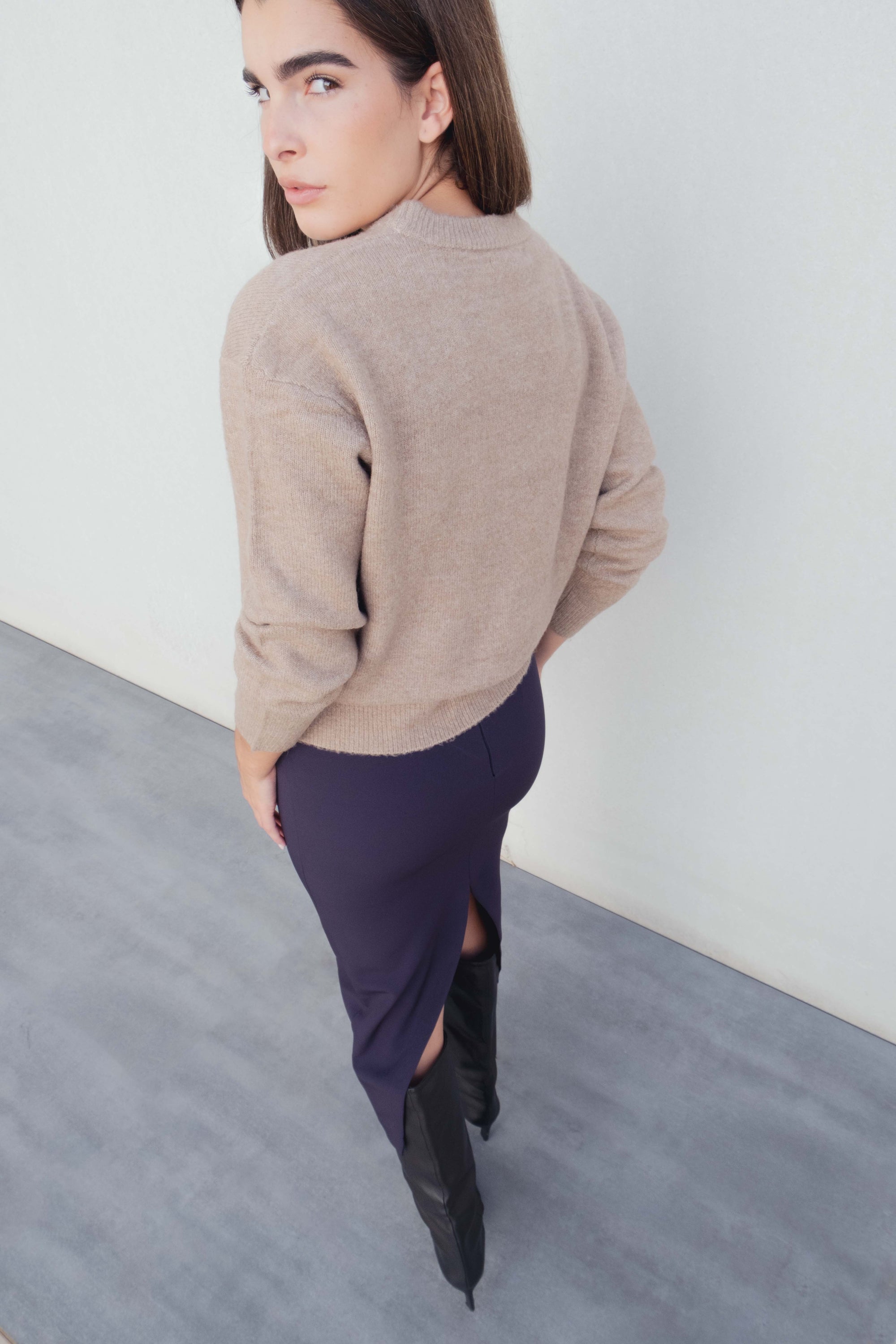 Vue arrière d'un modèle en jupe midi marine taille haute, associée à un pull beige, soulignant la coupe élégante de la jupe midi.
