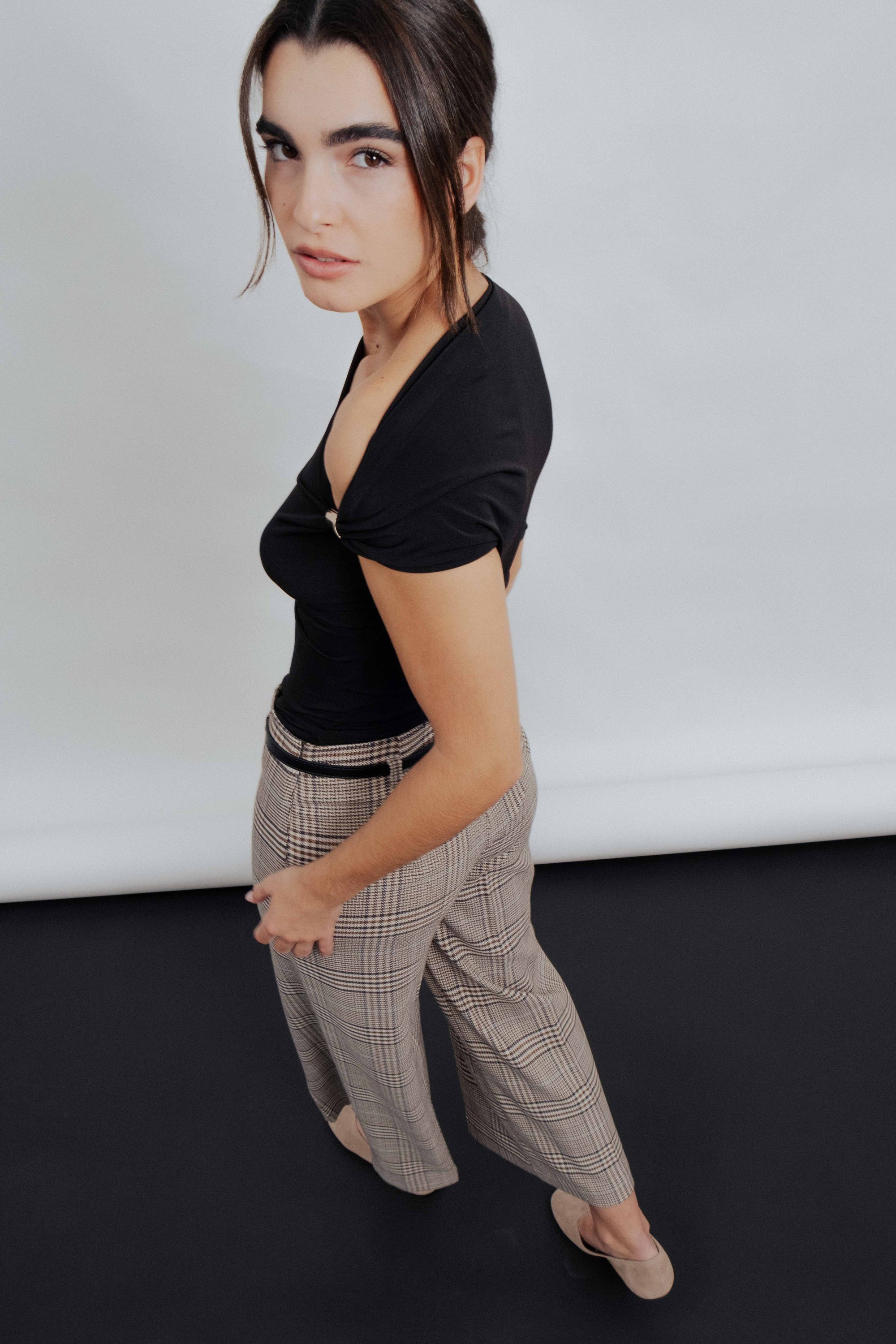 Femme dans un Pantalon culotte à carreaux marron, avec un haut noir, illustrant une tenue décontractée et stylée.