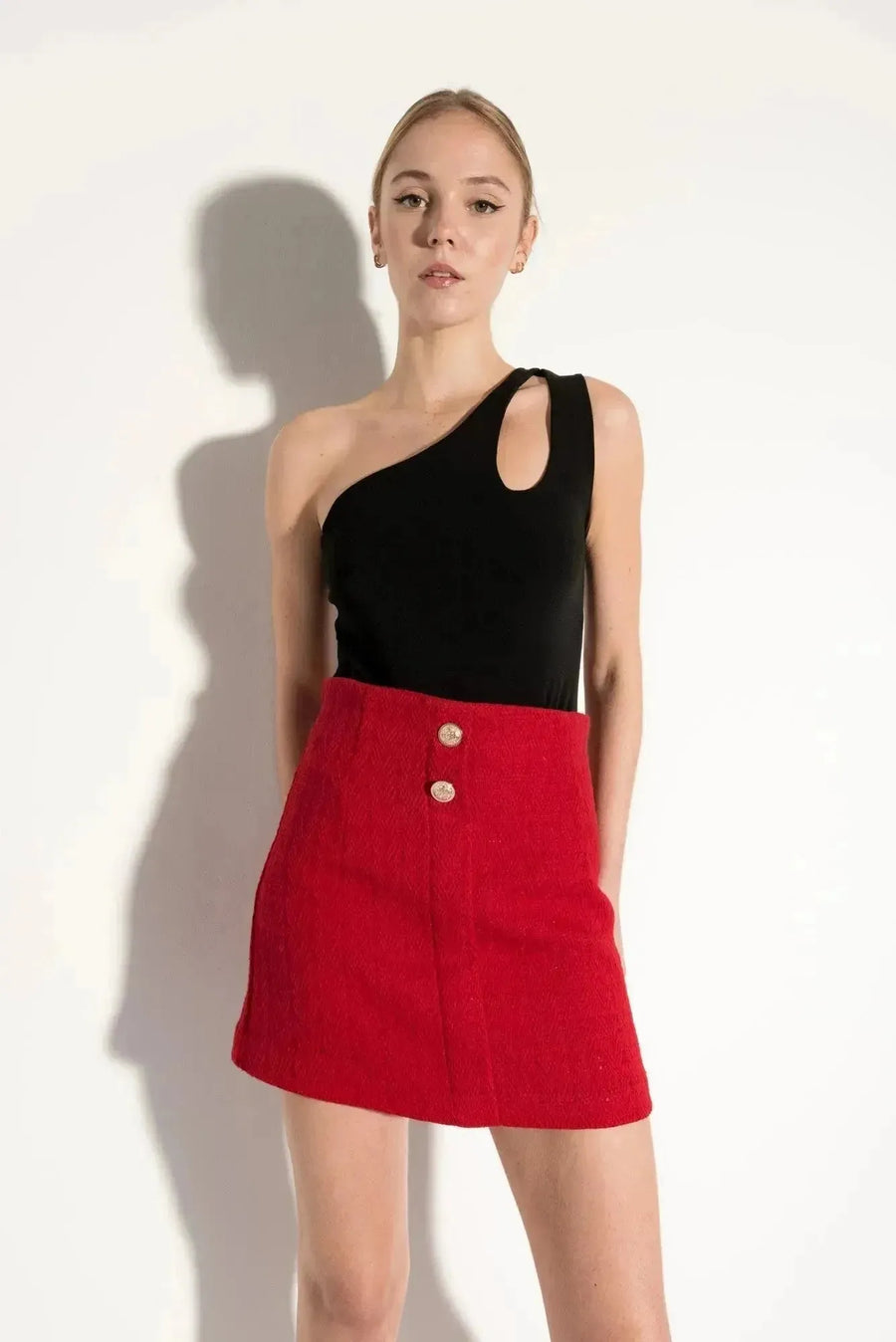 Modèle portant une jupe tweed femme avec découpe asymétrique et boutons dorés, parfaite pour un style chic et élégant.