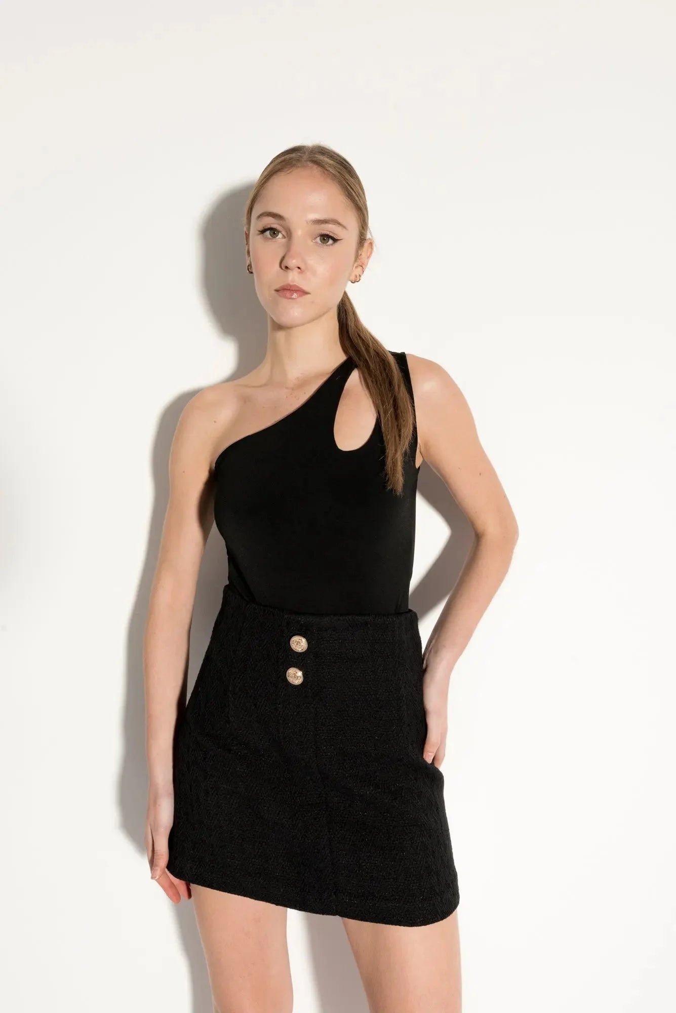 Femme portant une blouse noire asymétrique avec découpe et jupe en tweed à boutons dorés