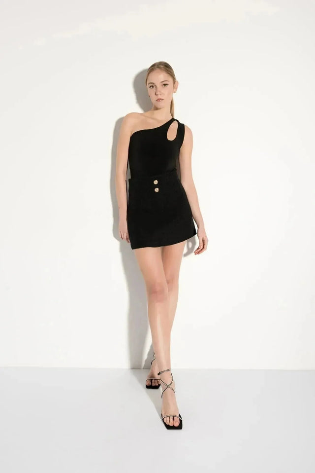 Femme en jupe tweed femme noire avec découpe asymétrique et boutons dorés, idéale pour un look tendance.