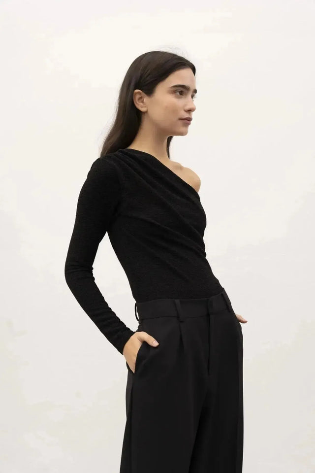 Modèle illustrant le design unique du body asymétrique, vêtu de façon chic, los d'un shooting photo en arrière-plan clair.