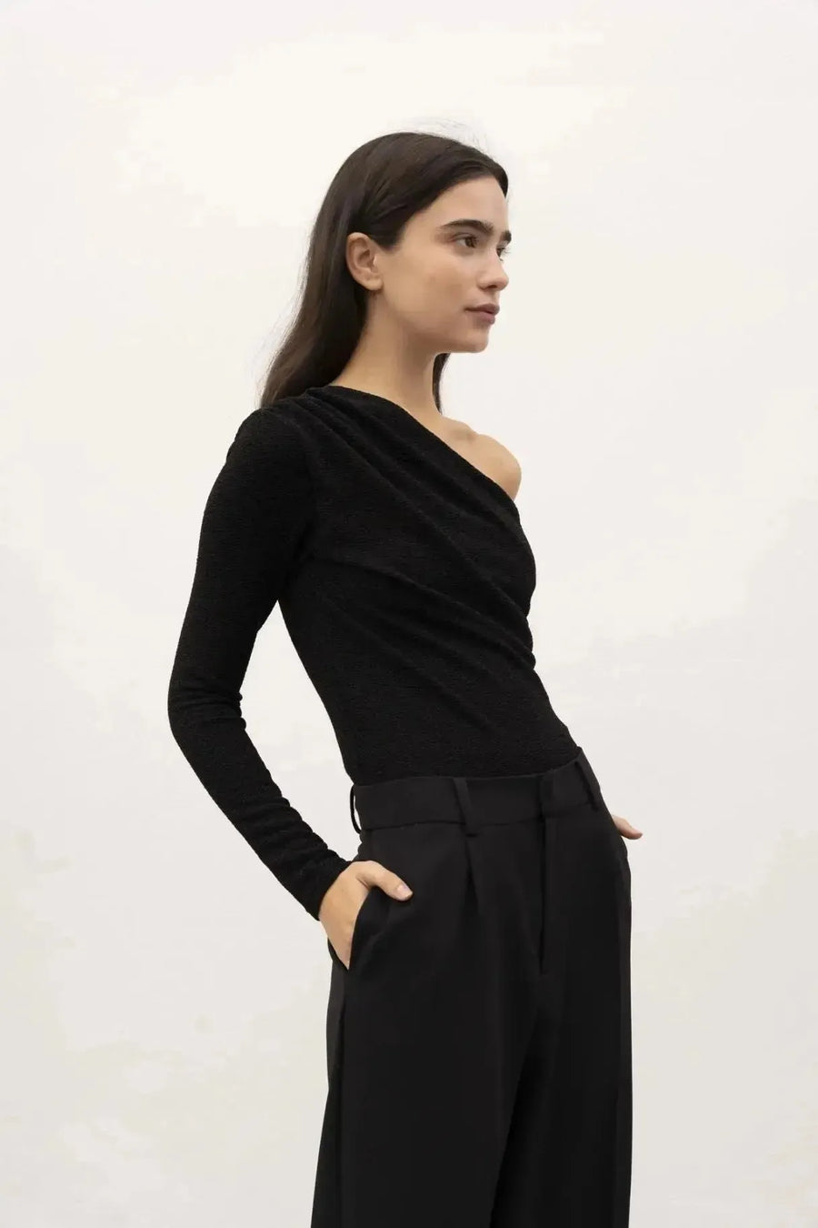 Modèle illustrant le design unique du body asymétrique, vêtu de façon chic, los d'un shooting photo en arrière-plan clair.