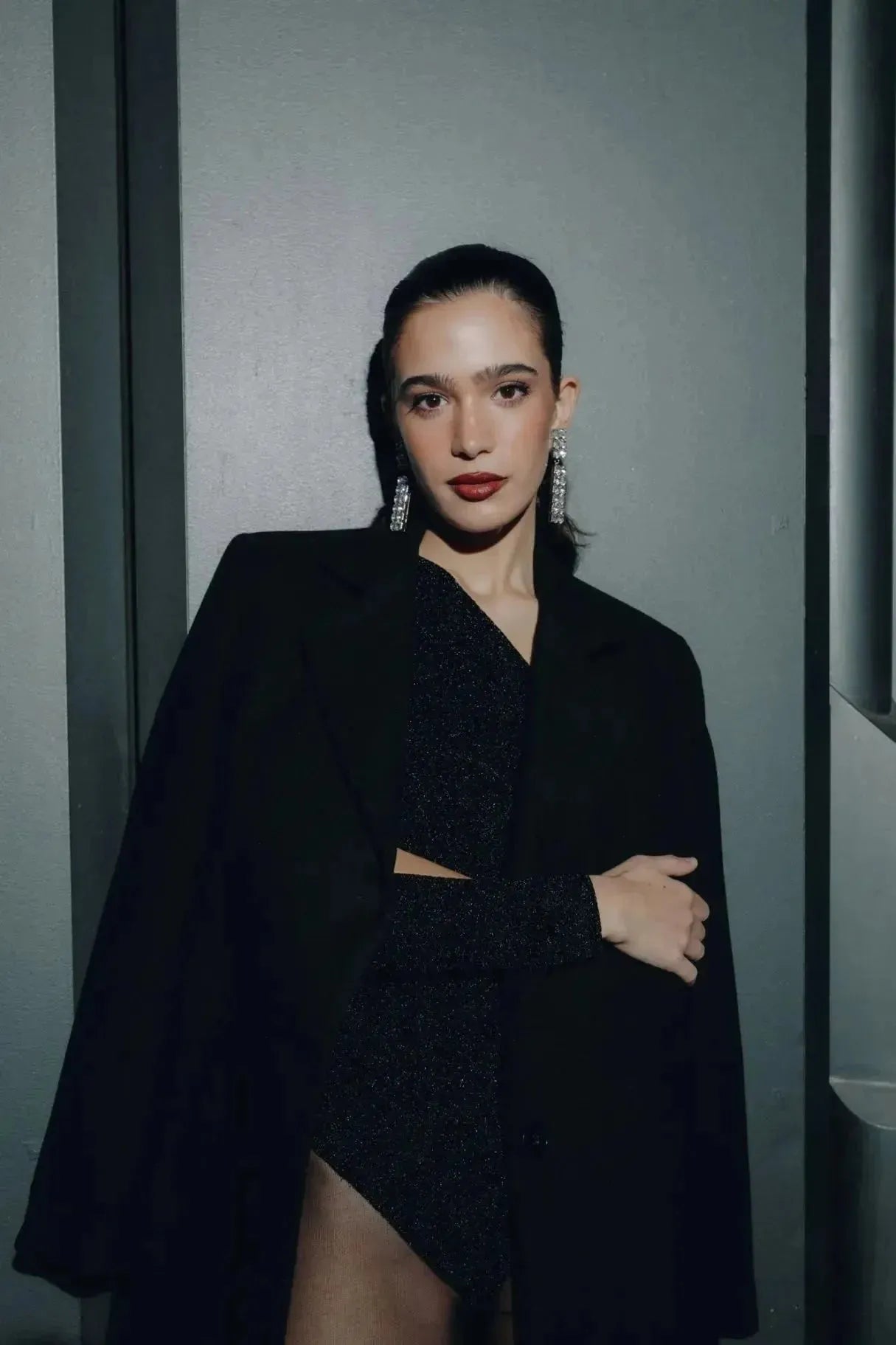 Modèle portant un ensemble avec body asymétrique au confort optimal, vêtu d'un blazer noir et d'une jupe scintillante, affichant un look chic et sophistiqué.