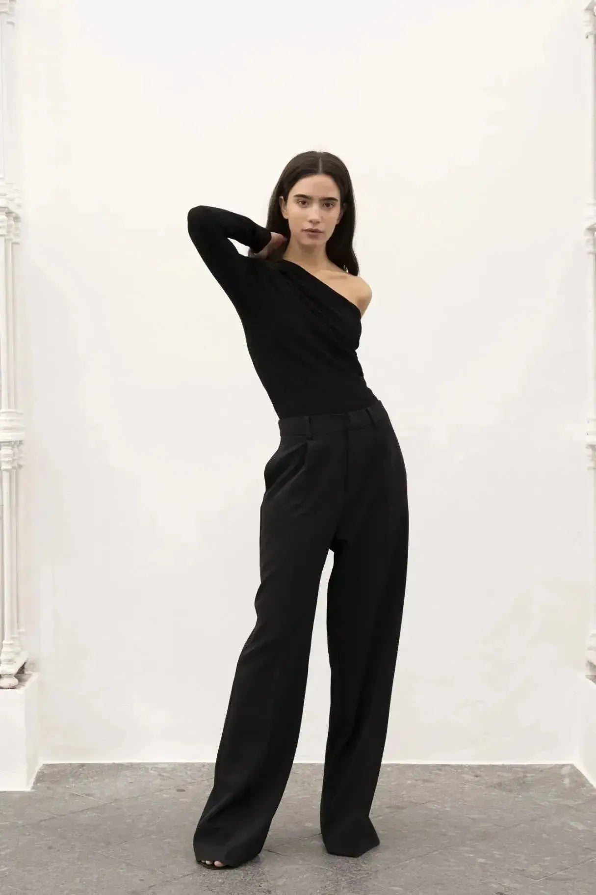 Vue profil d'un modèle en body asymétrique et pantalon noir, posant avec assurance pour mettre en avant la silhouette élégante.