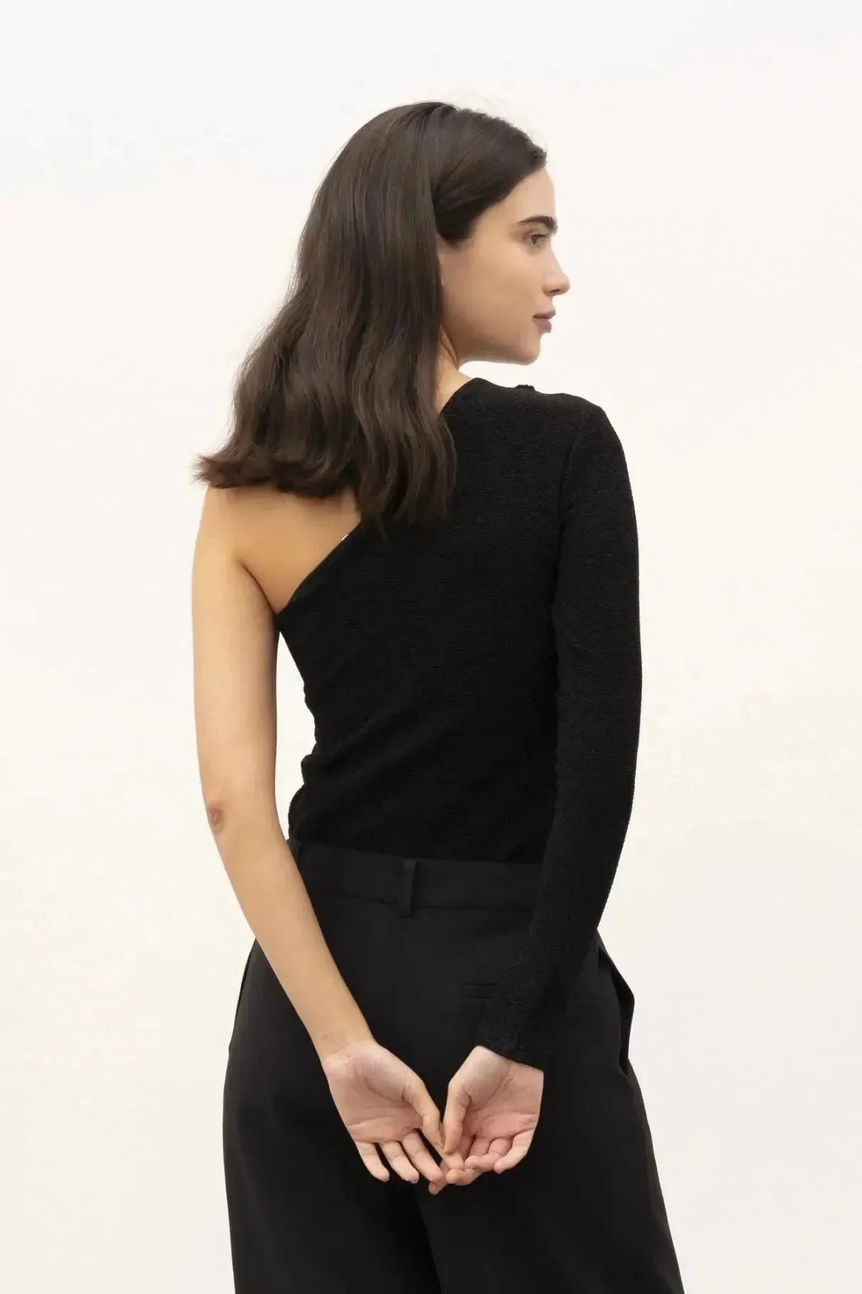 Modèle de dos, habillé d'un body asymétrique noir, illustrant le design innovant et moderne de la pièce.