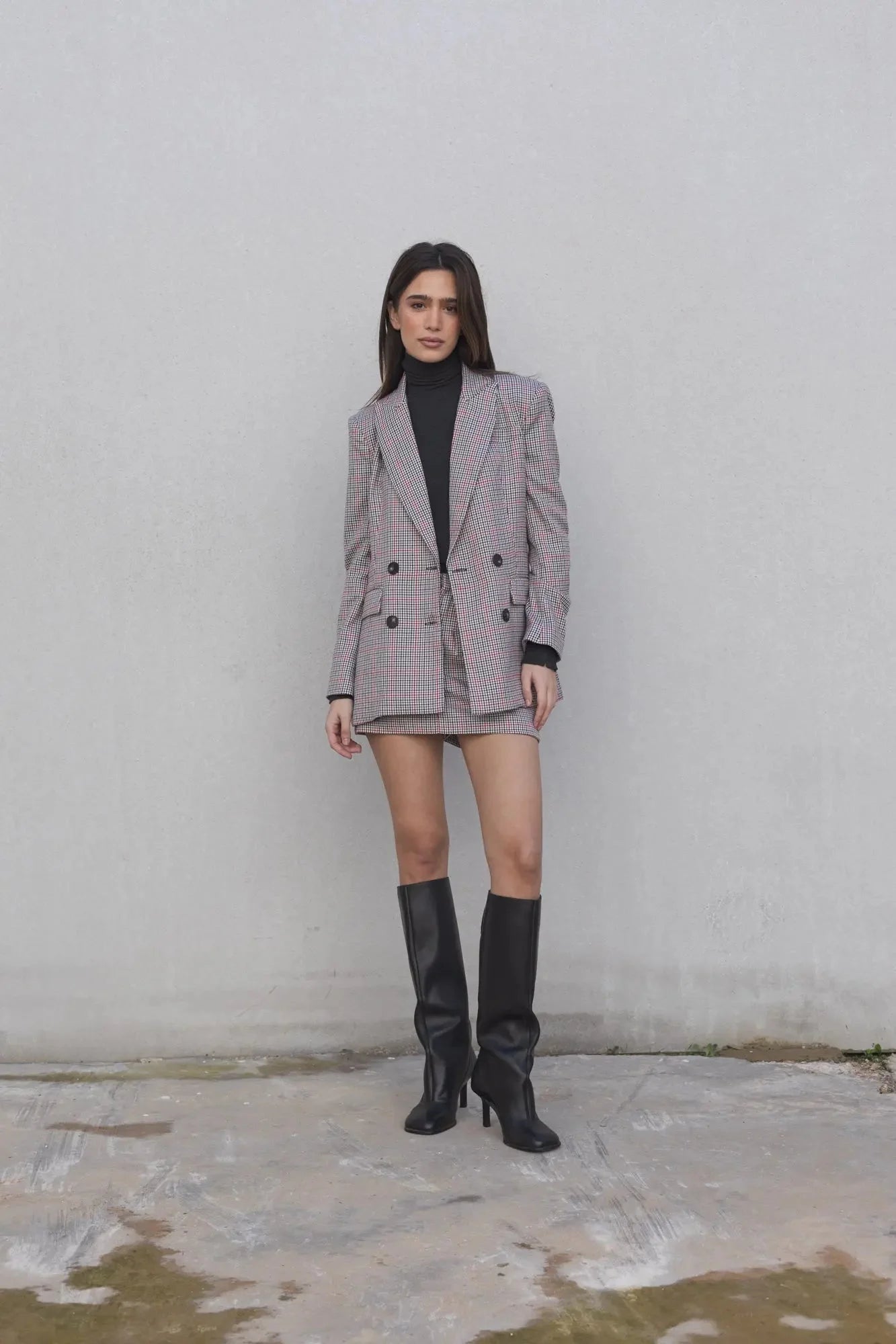 Modèle en pose portant le blazer femme double boutonnage à carreaux avec mini jupe élégante de Sapiato et bottes noires.