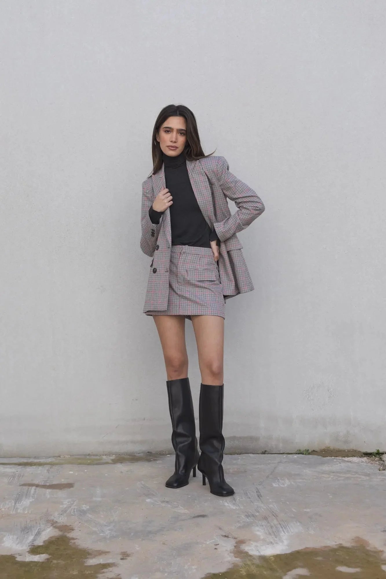 Modèle portant le blazer femme double boutonnage à carreaux avec mini jupe élégante de Sapiato, combiné avec des bottes noires.