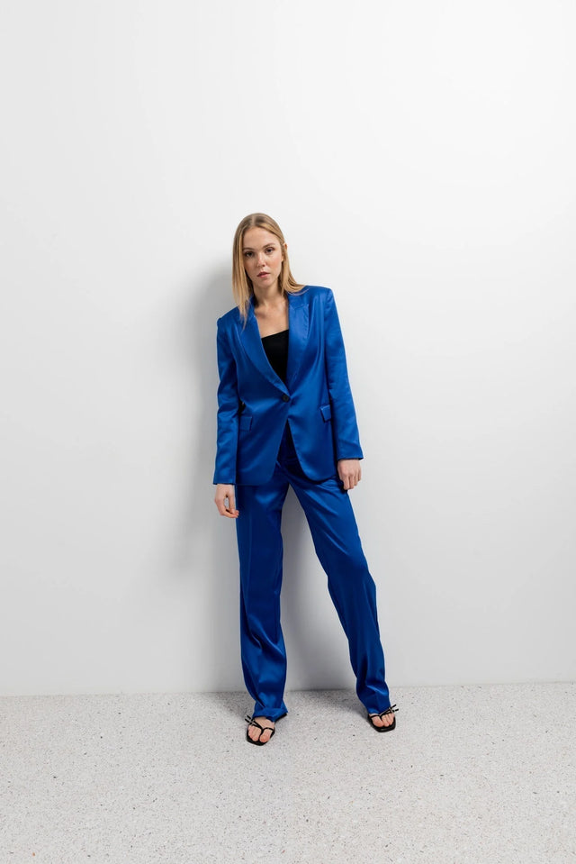 Femme en posture décontractée, affichant un blazer satiné bleu roi avec un pantalon assorti, un choix parfait pour une soirée stylée. Découvrez le blazer bleu roi femme, symbole d'élégance.