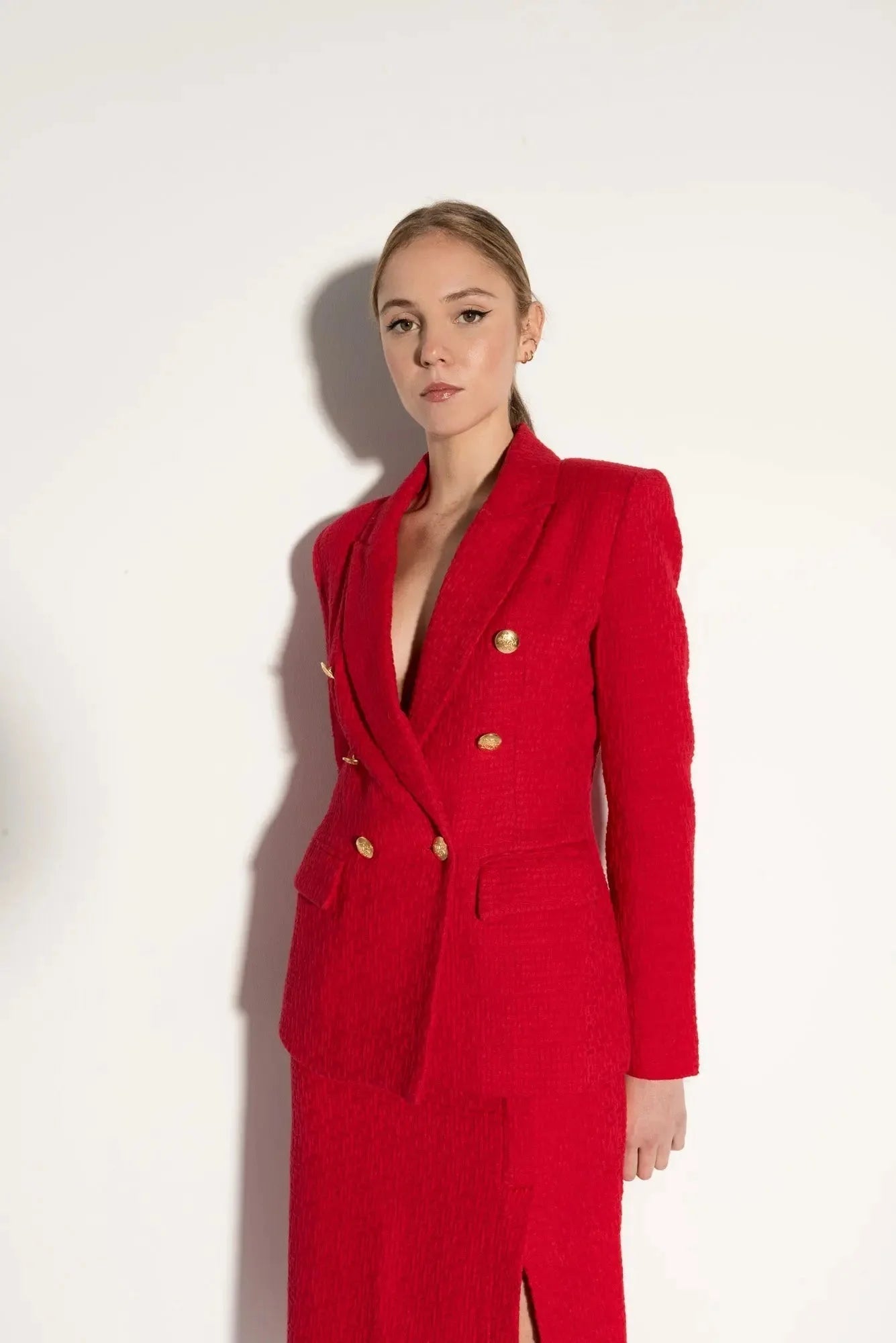 Femme portant un blazer texturé rouge vif avec boutons en or et jupe longue à fente