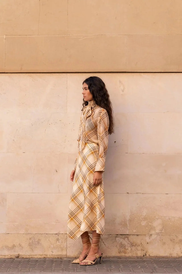 Femme posant côté à un mur avec un chemisier cravate femme à carreaux, soulignant la douceur de la matière.
