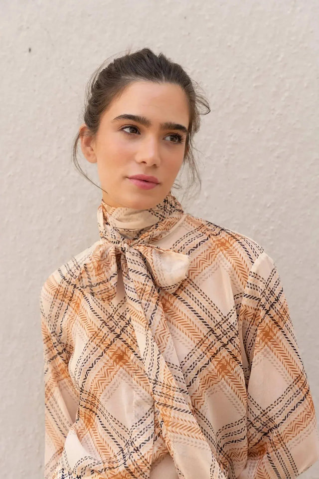 Gros plan sur une femme portant un chemisier cravate femme à carreaux, mettant en avant les détails raffinés du col lavallière.