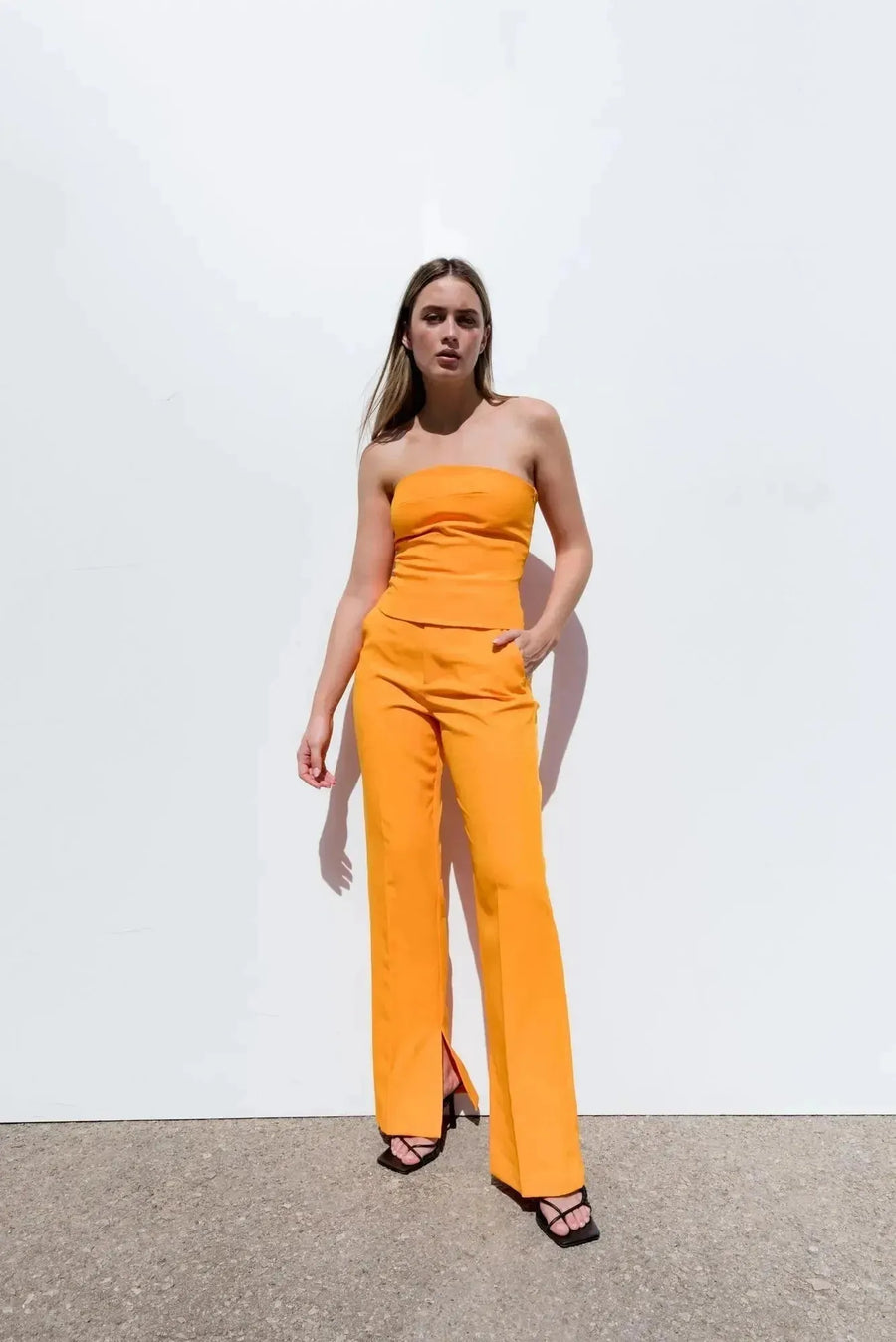 Modèle en top bandeau femme orange et pantalon fluide, posant avec assurance pour un style chic et contemporain.