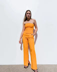 Modèle en top bandeau femme orange et pantalon fluide, posant avec assurance pour un style chic et contemporain.