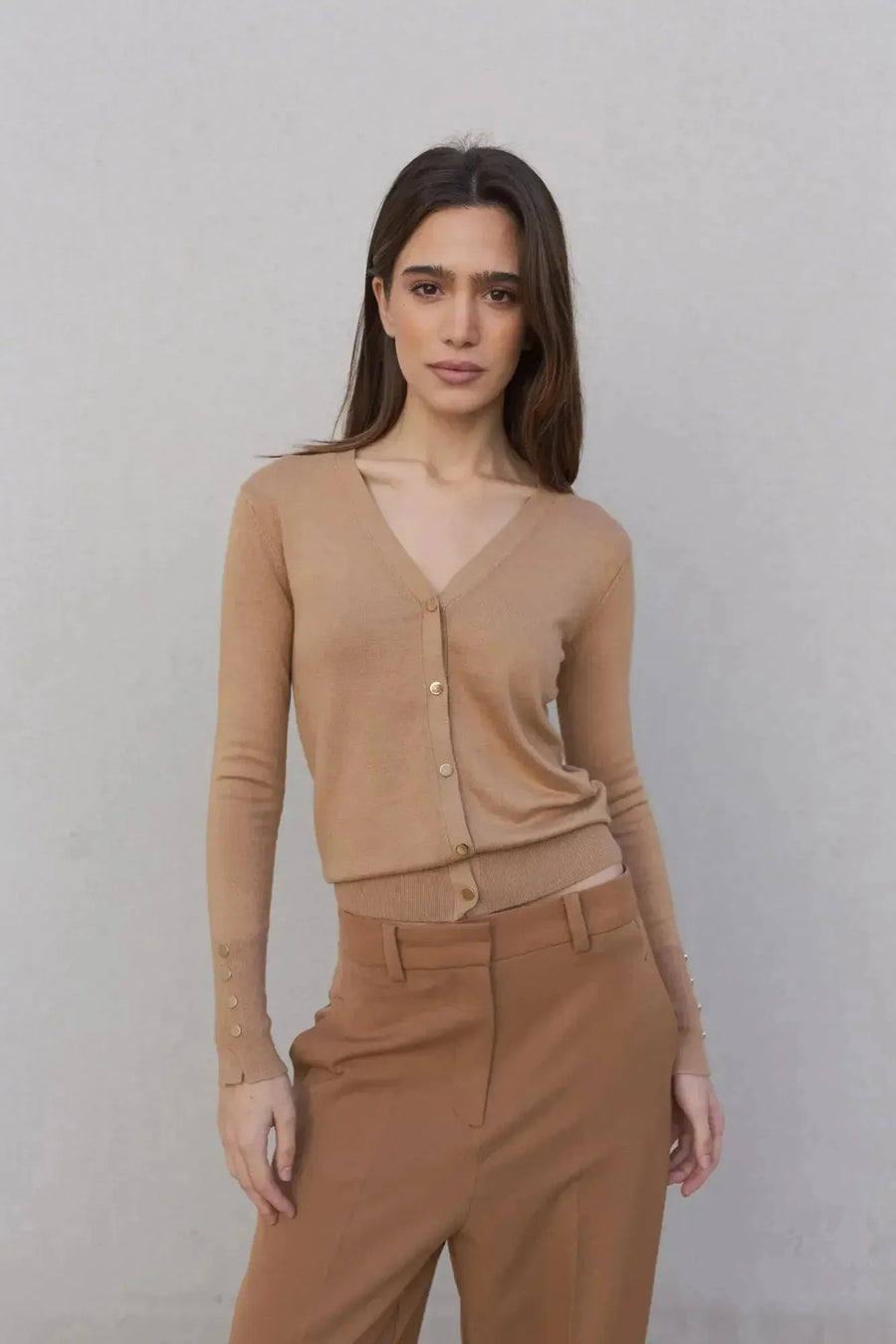 Femme souriante dans un gilet tricot femme beige, mettant en valeur le confort et l'élégance avec un pantalon marron.