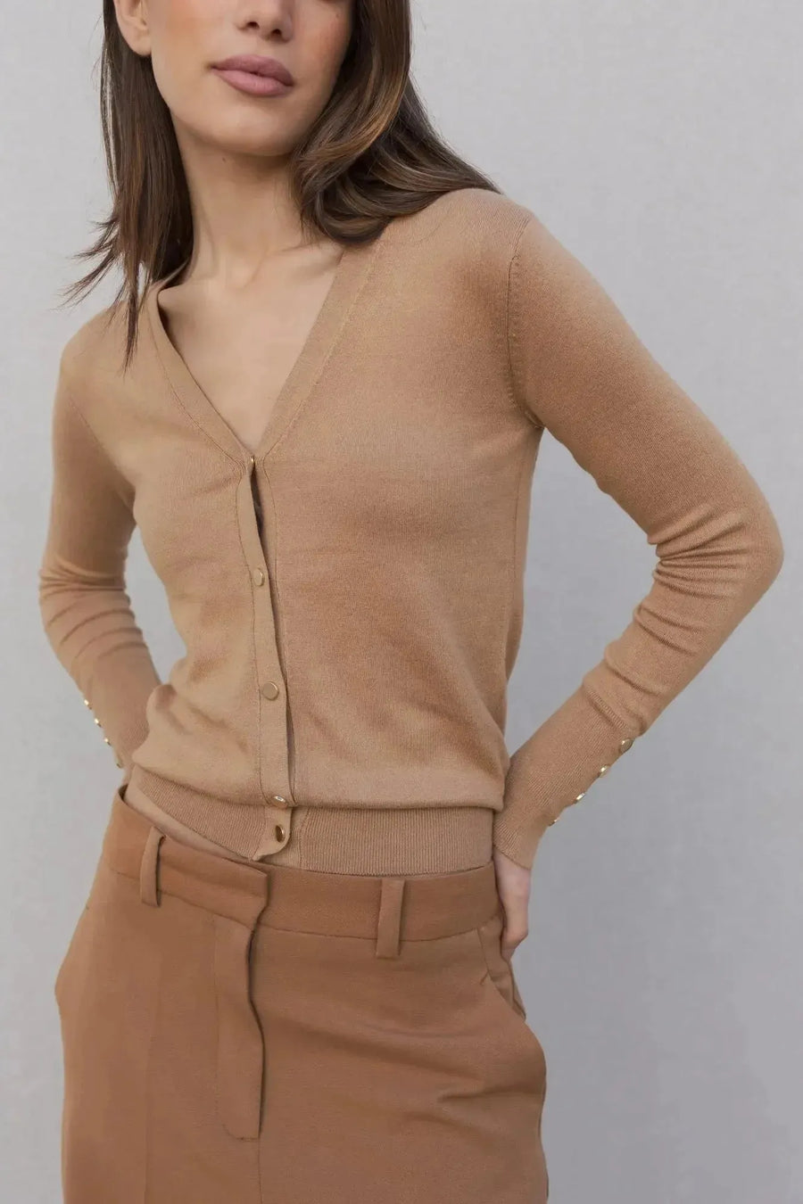 Femme portant un gilet tricot femme beige avec boutons, associé à un pantalon marron, illustration du style élégant et confortable.