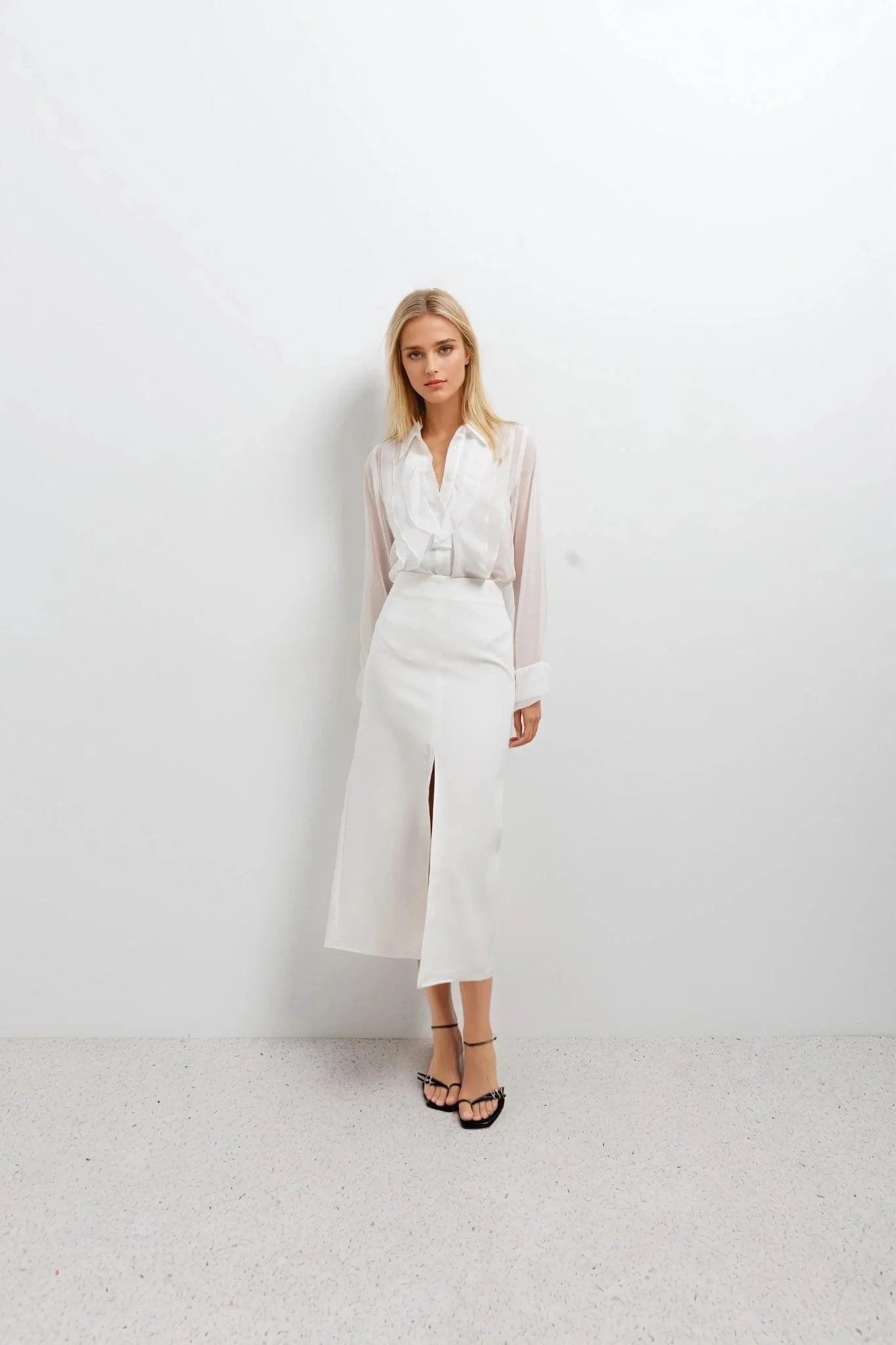 Femme portant une chemise à volants blanche et une jupe fendue midi, sandales noires
