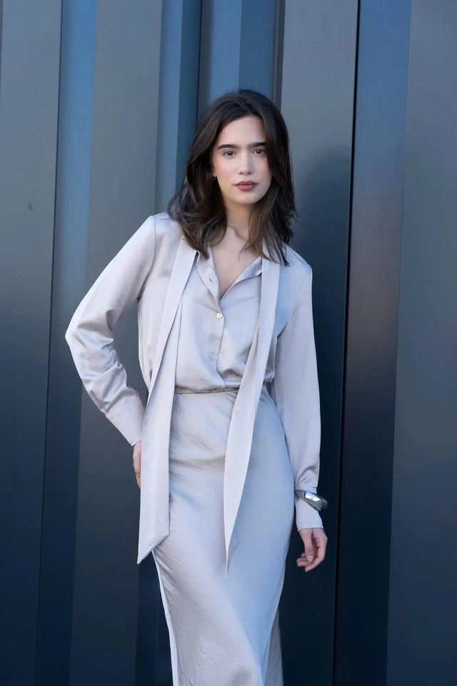 Femme dans une chemise lavallière femme fluide, montrant un style chic et décontracté, à côté d'une paroi en métal.