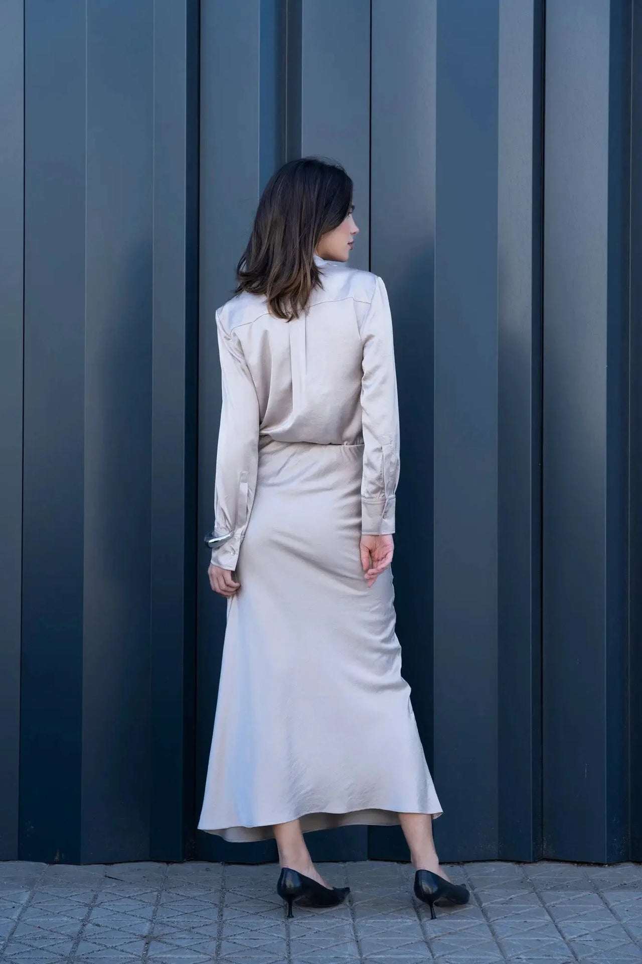 Vue arrière d'une femme en chemise lavallière femme fluide, soulignant l'élégance de la coupe devant une façade moderne.