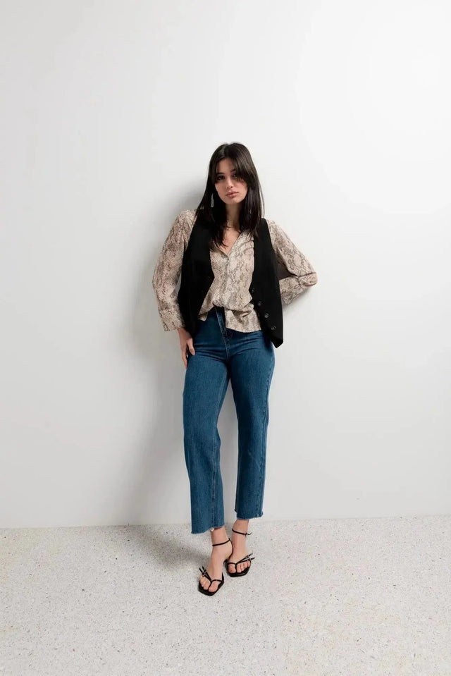 Femme stylée dans une chemise imprimée animal femme, portant un gilet noir et un jean pour un look décontracté.