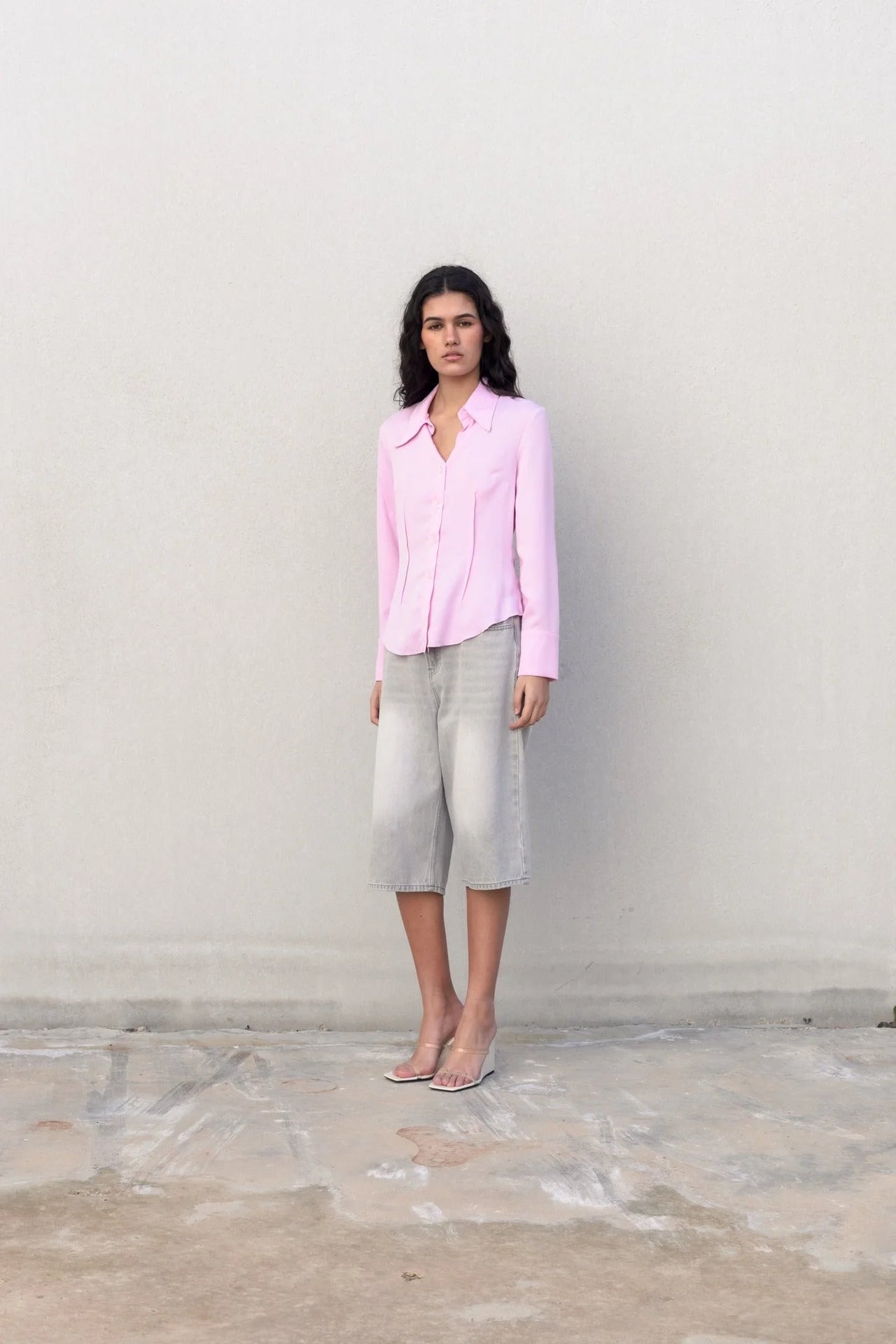 Modèle posant dans une chemise femme cintrée rose pastel, face à la caméra, avec une silhouette féminine soulignée.