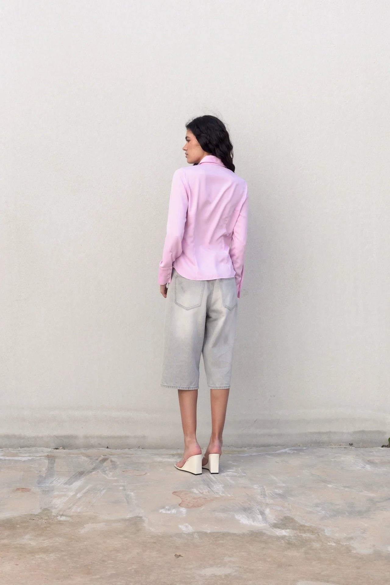Vue arrière d'un modèle portant une chemise femme cintrée rose pastel, associée à un look décontracté avec un short en denim.