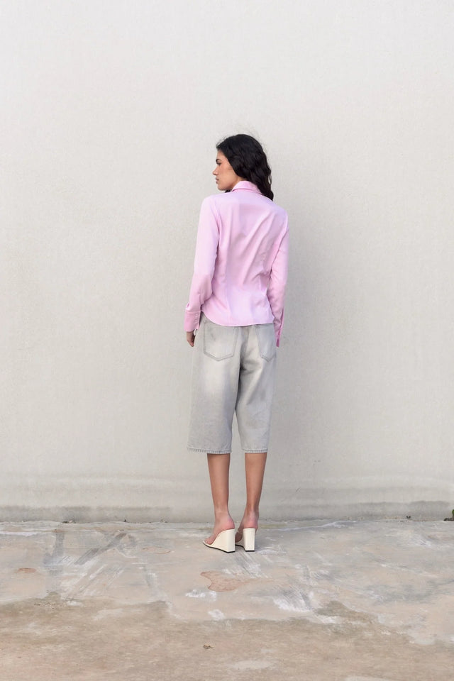 Vue arrière d'un modèle portant une chemise femme cintrée rose pastel, associée à un look décontracté avec un short en denim.