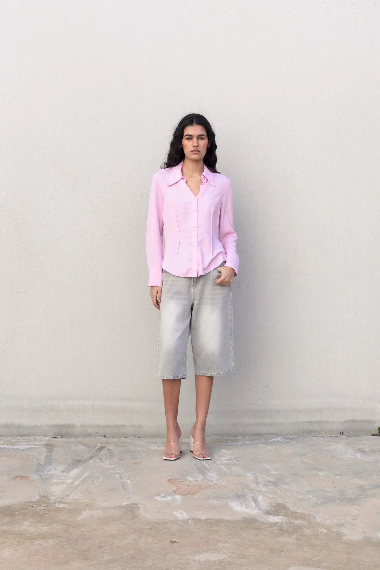 Femme décontractée en chemise femme cintrée rose pastel sur fond de mur neutre, mettant en avant le style chic.