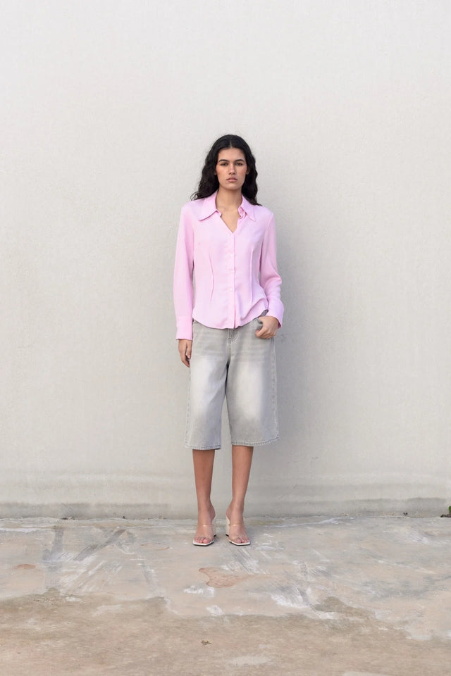 Femme décontractée en chemise femme cintrée rose pastel sur fond de mur neutre, mettant en avant le style chic.